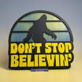 RJ Custom Works layered wood sign with black Bigfoot silhouette over a retro sunset background and yellow "Don't Stop Believin'" text.